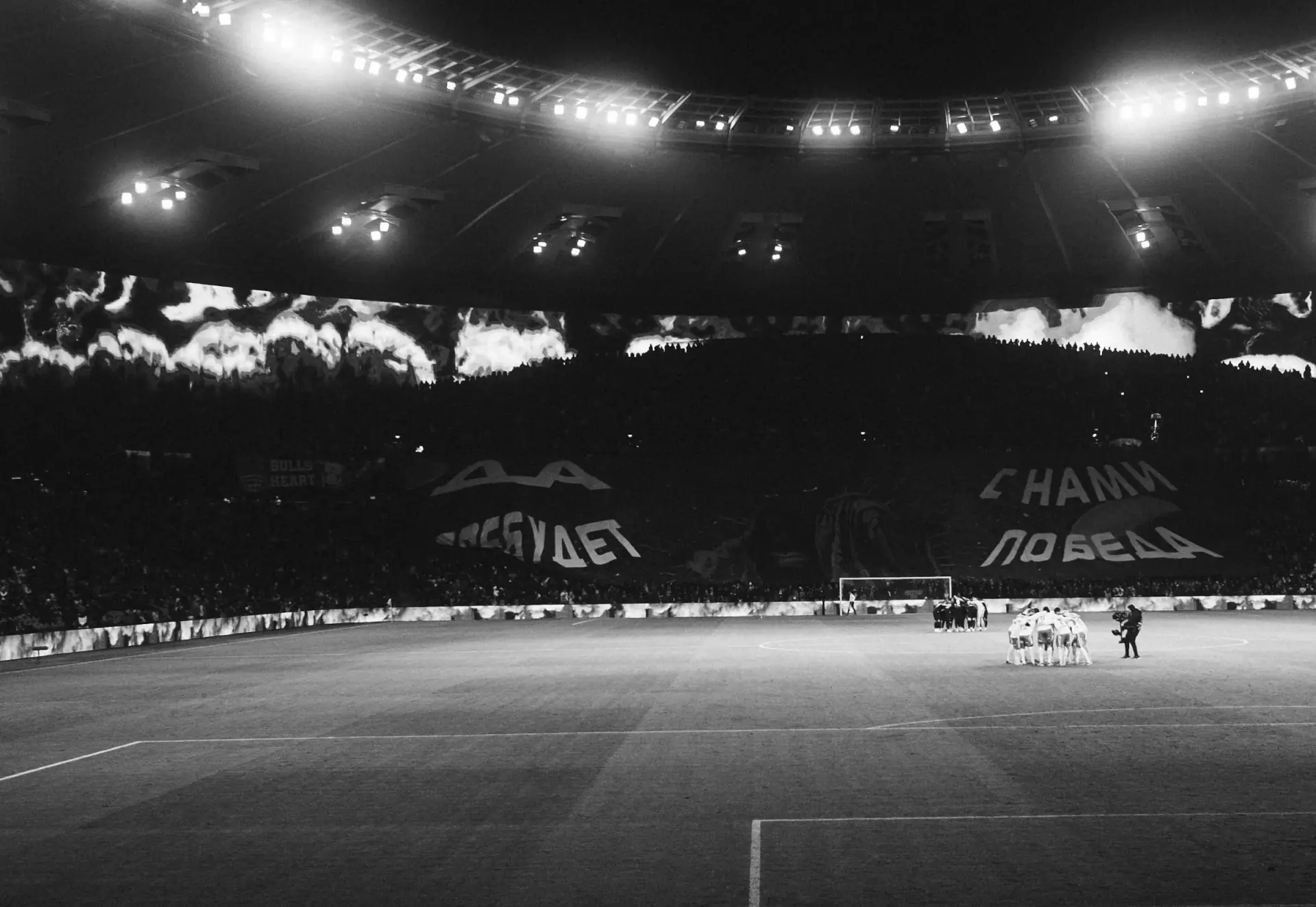A floodlit football stadium filled with supporters at night